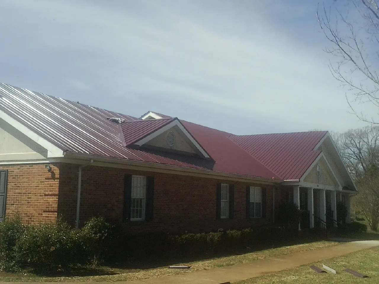 Red metal roof with gabled entries on a long brick building, from a Hail Damage Roof Repair job in Derry