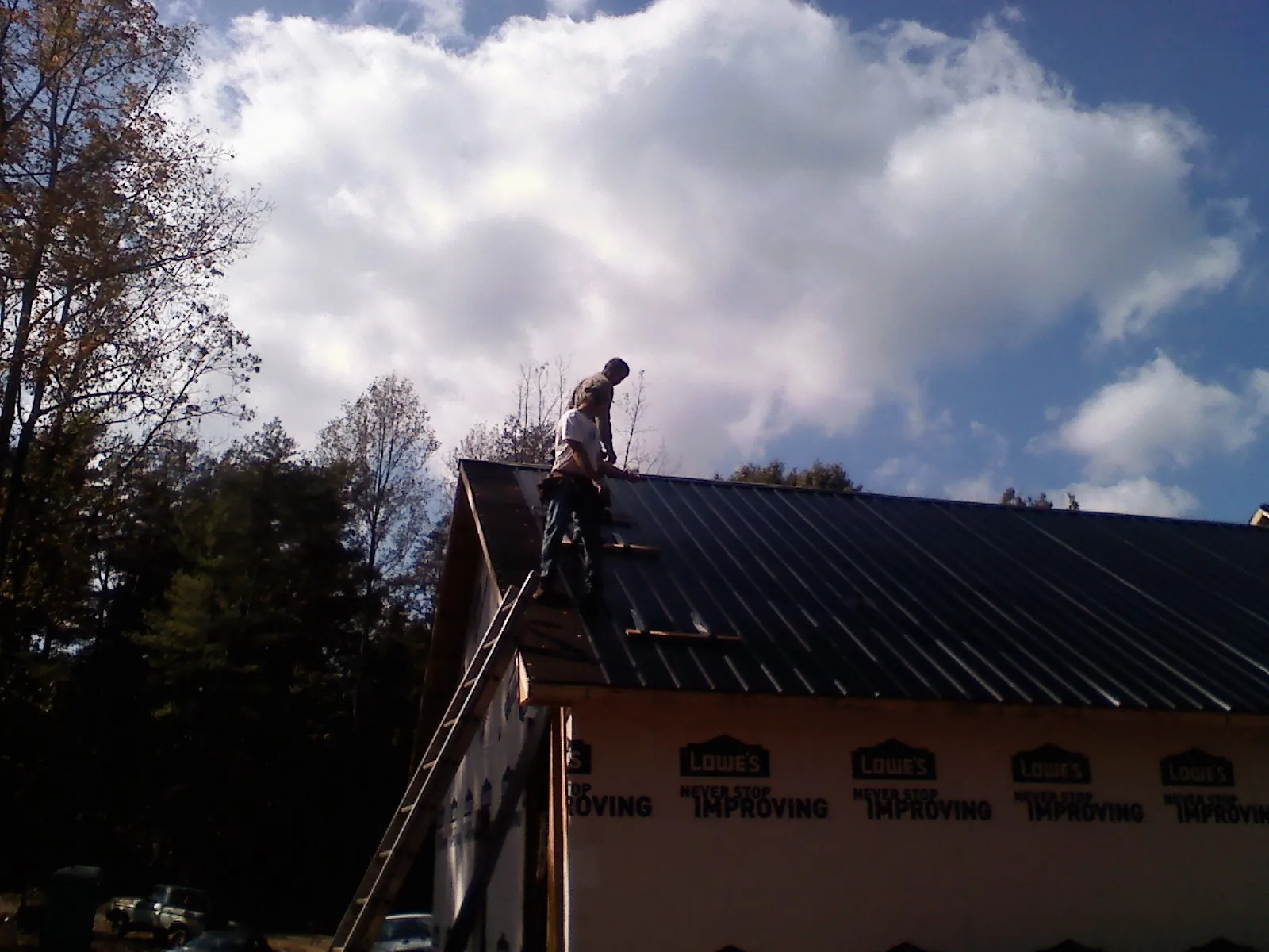 Roofer fastening dark metal panels high against a cloudy sky, from a Roof Inspection job in Derry