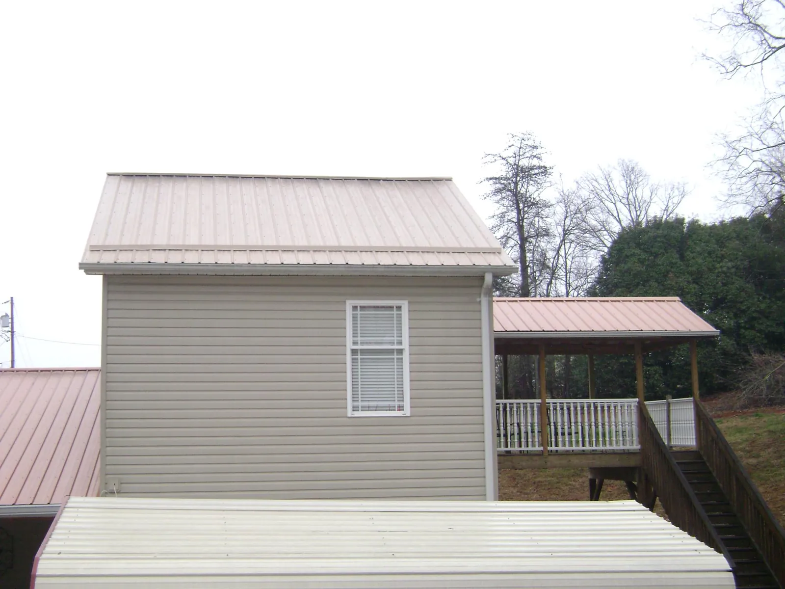 Tan metal roofs on a two story addition and attached porch, from a Roof Replacement job in Derry